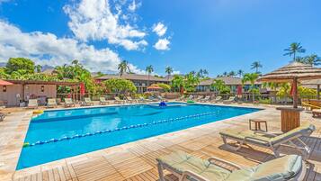 A pool area with lounge chairs and umbrellas, surrounded by palm trees and buildings.