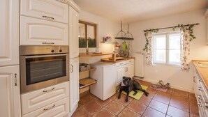 A kitchen with white cabinets, a built-in oven, a small refrigerator, and a dog lying on a mat. - Exclusive vacation in the historic building in Chiemgau   (Traunstein)