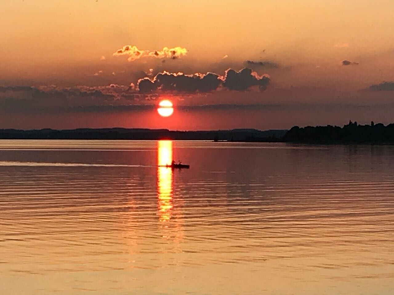 A sunset over a calm body of water with a silhouette of a boat in the foreground.
