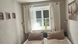 A bedroom with two single beds, a window with curtains, a radiator, and a wall-mounted light fixture. - Exclusive vacation in the historic building in Chiemgau   (Traunstein)
