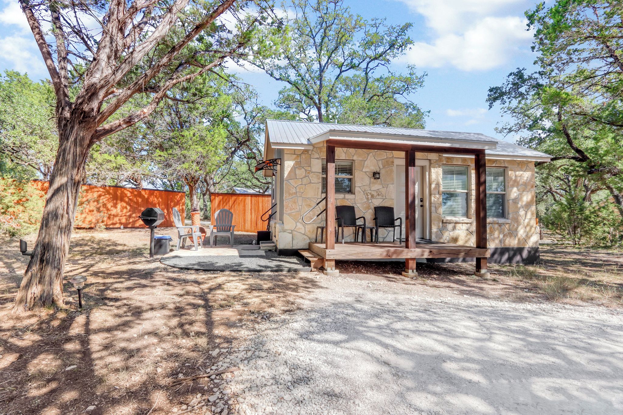 A small stone cabin with a porch, outdoor seating, and a fenced area.