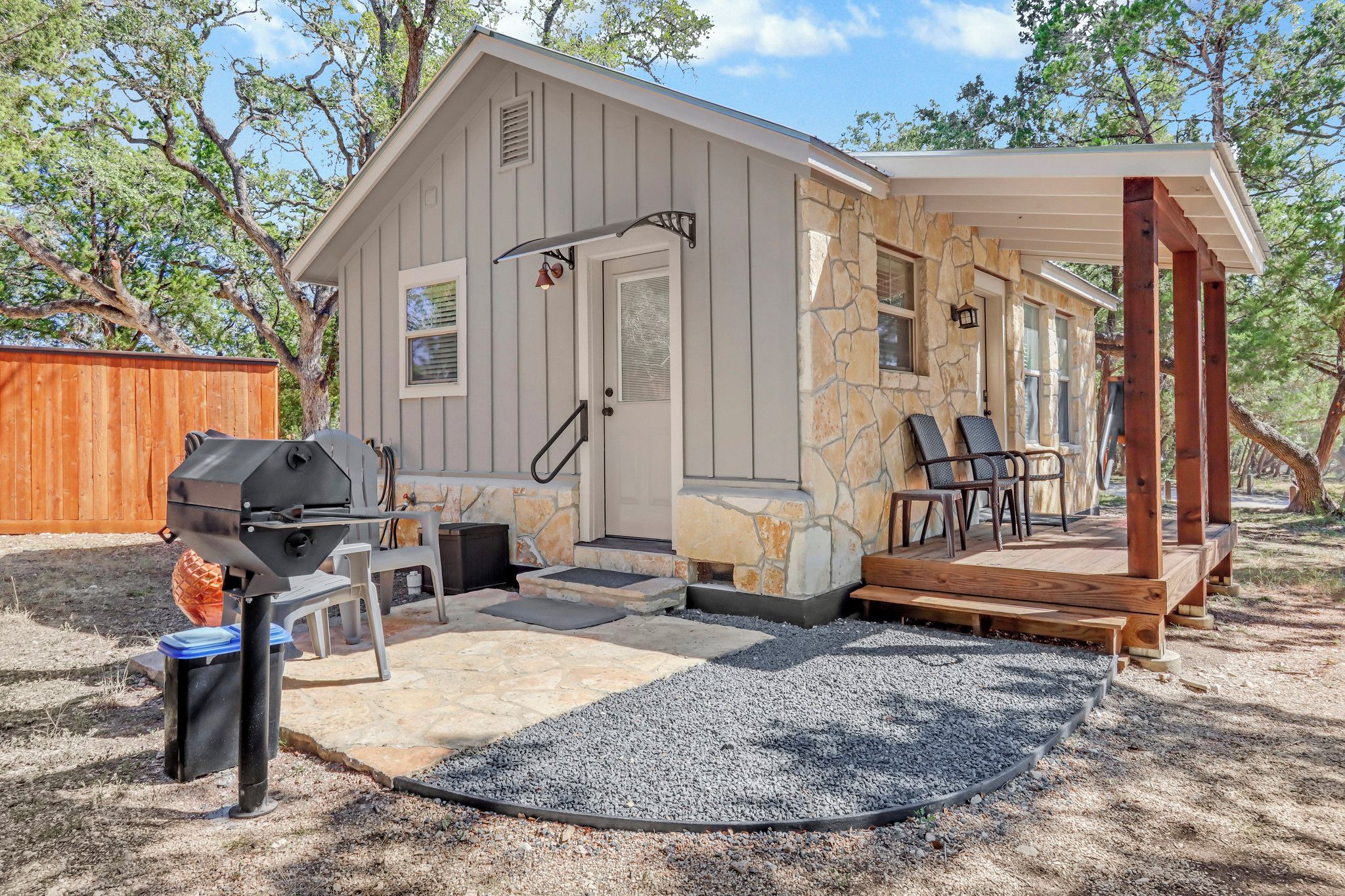 A small cabin with a stone exterior, a porch with seating, and a barbecue grill.
