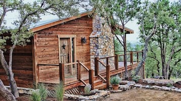 A rustic cabin with a stone chimney, wooden deck, and a star-shaped window.