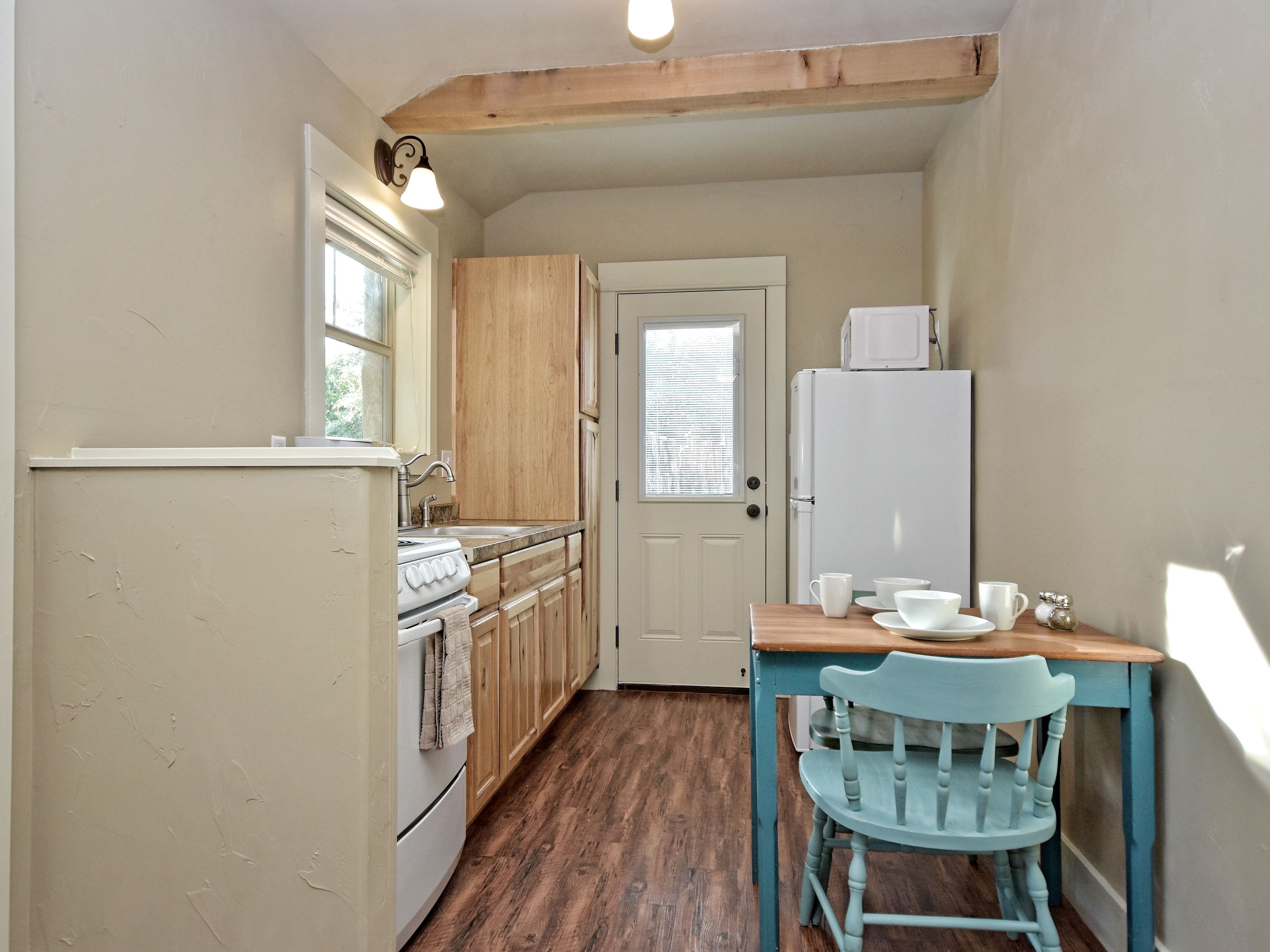 Una cocina compacta con armarios de madera, un refrigerador blanco, una estufa y una mesa de comedor con una silla azul.