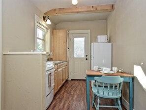 Eine kleine Küche mit Holzschränken, einem weißen Kühlschrank, einem Herd und einem Esstisch mit blauem Stuhl.