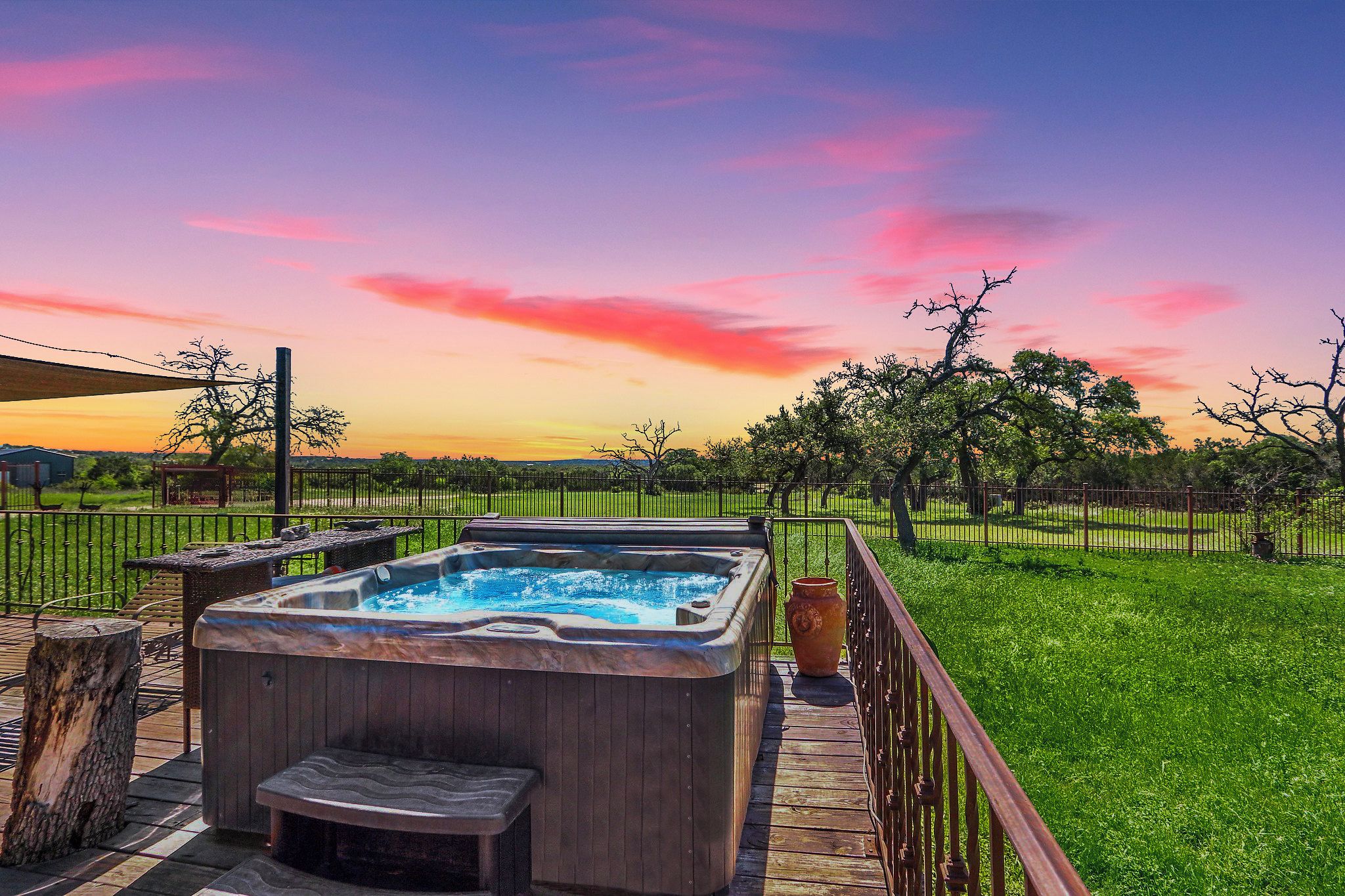 A hot tub on a wooden deck with a view of a grassy field and trees.