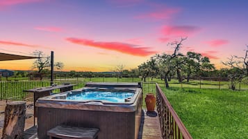 A hot tub on a wooden deck with a view of a grassy field and trees.