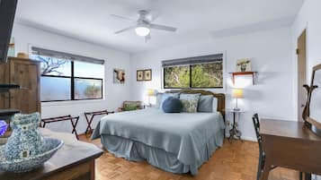 A bedroom with a bed, a ceiling fan, a window, a lamp, and a wooden table.