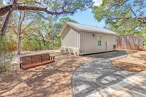 A small wooden cabin with a porch, surrounded by trees and a gravel path. - Morning Dove I Romantic, Minutes from The Square! (Wimberley)