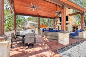 An outdoor patio with a covered seating area, stone fireplace, and a view of a house in the background. - Morning Dove I Romantic, Minutes from The Square! (Wimberley)