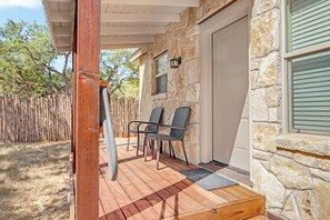 A covered porch with stone walls, two wicker chairs, and a wooden bench. - Morning Dove I Romantic, Minutes from The Square! (Wimberley)