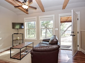 A living room with a brown leather sofa, a wooden coffee table, a TV mounted on the wall, and a ceiling fan.