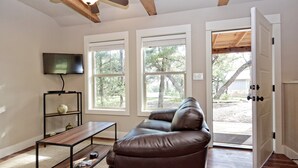 A living room with a brown leather sofa, a wooden coffee table, a TV mounted on the wall, and a ceiling fan. - HCPL-Mockingbird I Cabin, Close to Wimbeley Square! (Wimberley)