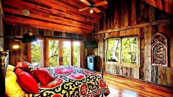 A wooden cabin bedroom with a bed, a ceiling fan, and large windows.