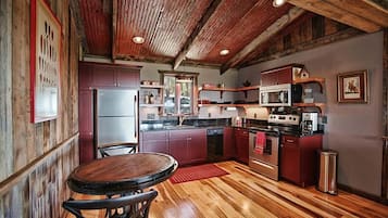 A rustic kitchen with wooden floors, a round dining table, and a refrigerator.