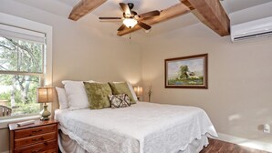 A bedroom with a wooden ceiling, a bed with white bedding, a nightstand, a lamp, and a painting on the wall. - HCPL-Mockingbird I Cabin, Close to Wimbeley Square! (Wimberley)