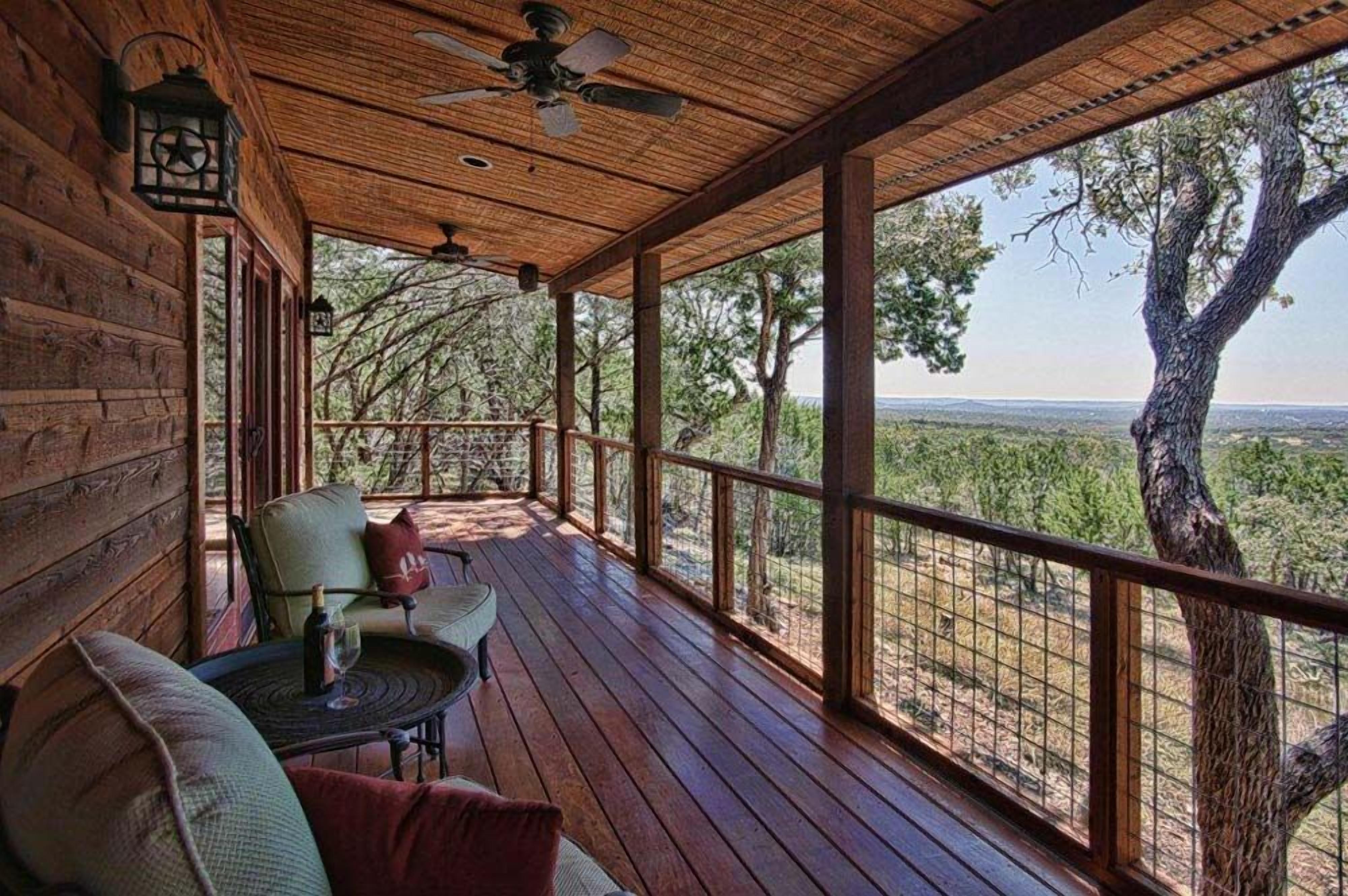 Una terraza de madera con una mesa y sillas, un ventilador de techo y vistas del paisaje circundante.