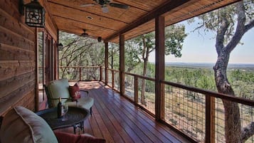 A wooden deck with a table and chairs, a ceiling fan, and a view of the surrounding landscape.