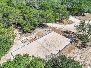 An aerial view of a sandy sports court with blue lines, surrounded by dense green trees. - HCPL-Mockingbird I Cabin, Close to Wimbeley Square! (Wimberley)