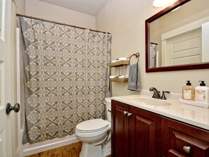 A bathroom with a patterned shower curtain, a toilet, a sink with a mirror above it, and a towel rack. - Mountain Laurel I 2Br Cabin near Square! (Wimberley)