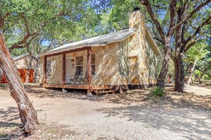 A rustic stone building with a porch, surrounded by trees. - Mountain Laurel I 2Br Cabin near Square! (Wimberley)
