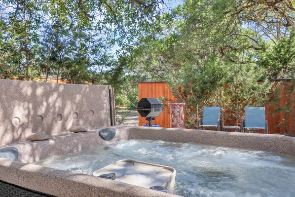 A hot tub with a stone surround, a grill, and two lounge chairs. - Mountain Laurel I 2Br Cabin near Square! (Wimberley)