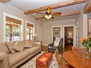 A living room with a beige sofa, a wooden coffee table, a wooden dining table, and a ceiling fan.