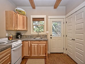 A kitchen with wooden cabinets, a stove, a sink, and a window with a view of trees.
