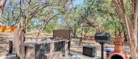 An outdoor patio with a stone barbecue grill, a terracotta pot, and a wooden pergola.