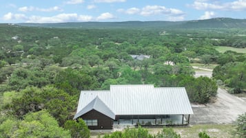 A modern building with a metal roof, surrounded by dense greenery and hills in the background.