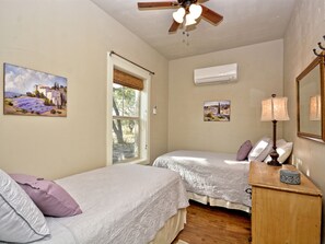 A bedroom with two beds, a ceiling fan, an air conditioning unit, and a wooden dresser. - Mountain Laurel I 2Br Cabin near Square! (Wimberley)