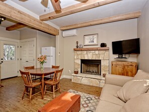 Una sala de estar con chimenea de piedra, muebles de madera, un televisor y una puerta que da a una cocina.
