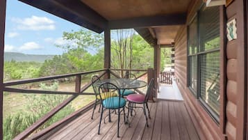 A covered outdoor area with a table and chairs, a railing, and a view of the surrounding landscape.