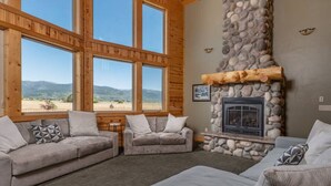 Ein gemütliches Wohnzimmer mit Kamin aus Stein, großen Fenstern und Blick auf die Berge.