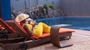 A poolside area with lounge chairs and a person relaxing by the pool.