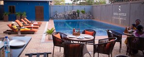 A poolside area with lounge chairs, a dining table, and a sign for Sonia Hotels. - Hotel Sonia (Ouagadougou)