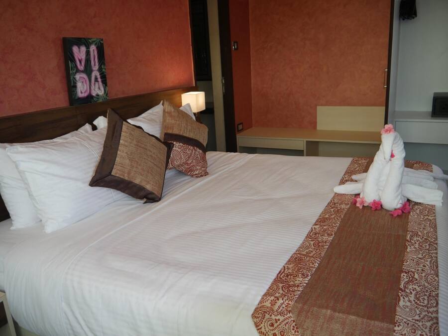 A hotel room with a large bed, pillows, a bedside table, a lamp, and a towel art piece on the bed.
