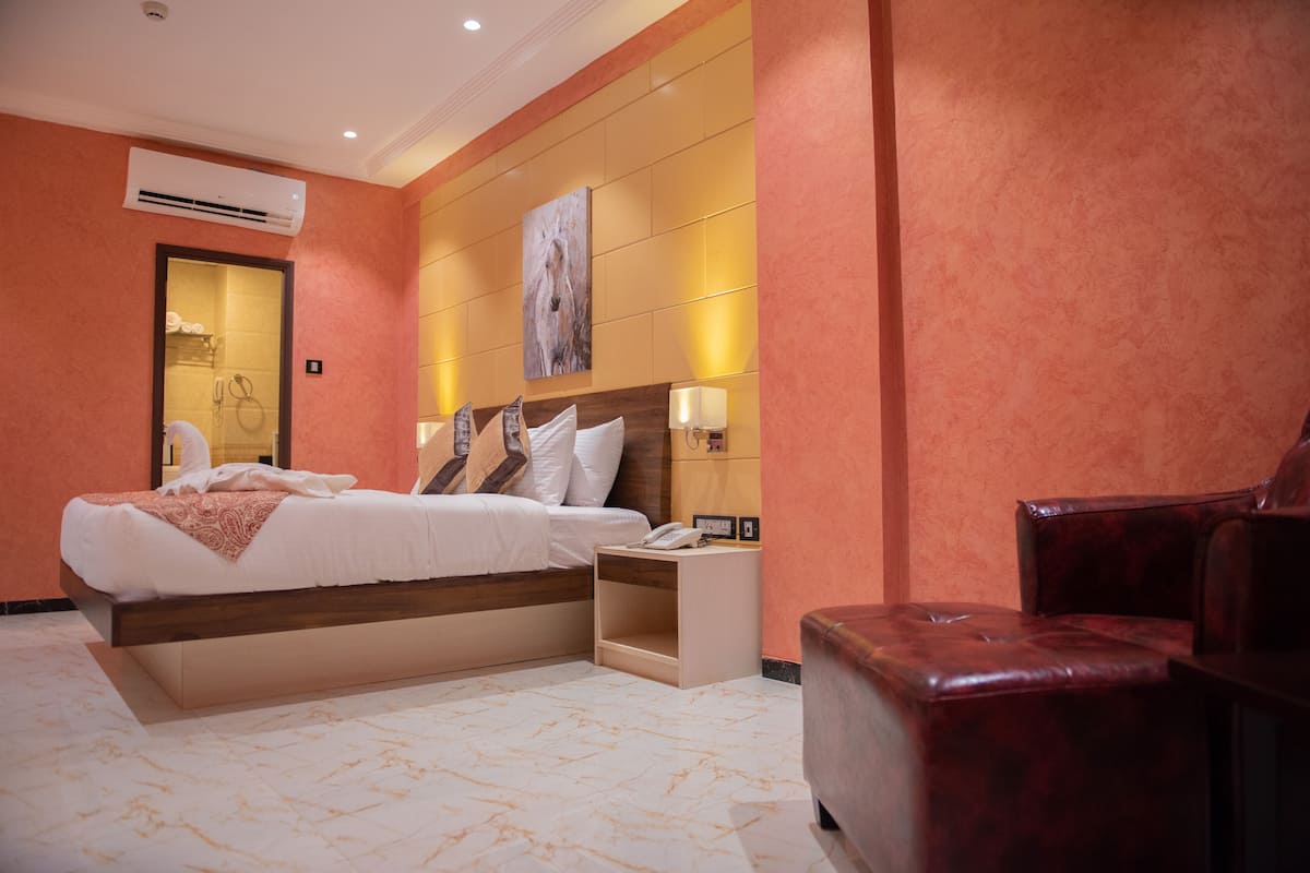 A hotel room with a bed, bedside table, lamp, and a leather armchair.