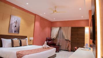 Une chambre d’hôtel avec un grand lit, un bureau, une chaise, un ventilateur de plafond et un tableau au mur.