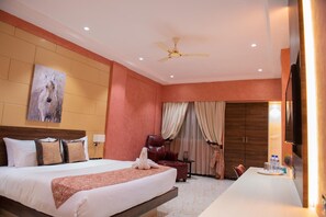 A hotel room with a large bed, a desk, a chair, a ceiling fan, and a painting on the wall. - Hotel Sonia (Ouagadougou)