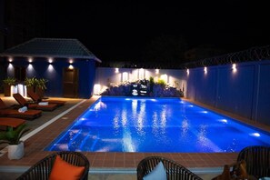 A swimming pool with a waterfall feature, surrounded by lounge chairs and potted plants. - Hotel Sonia (Ouagadougou)