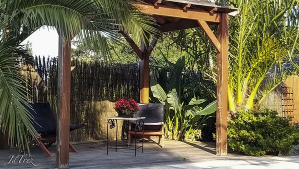 Une pergola en bois, agrémentée d’une table et de chaises, entourée d’une végétation tropicale luxuriante.