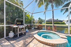 Eine Terrasse im Freien mit Grill, Pool und Palmen.