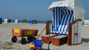 A beach chair with a striped canopy, a toy truck, and a small blue container on the sand. - Vacation cottage Stern, Germany (Wittmund)