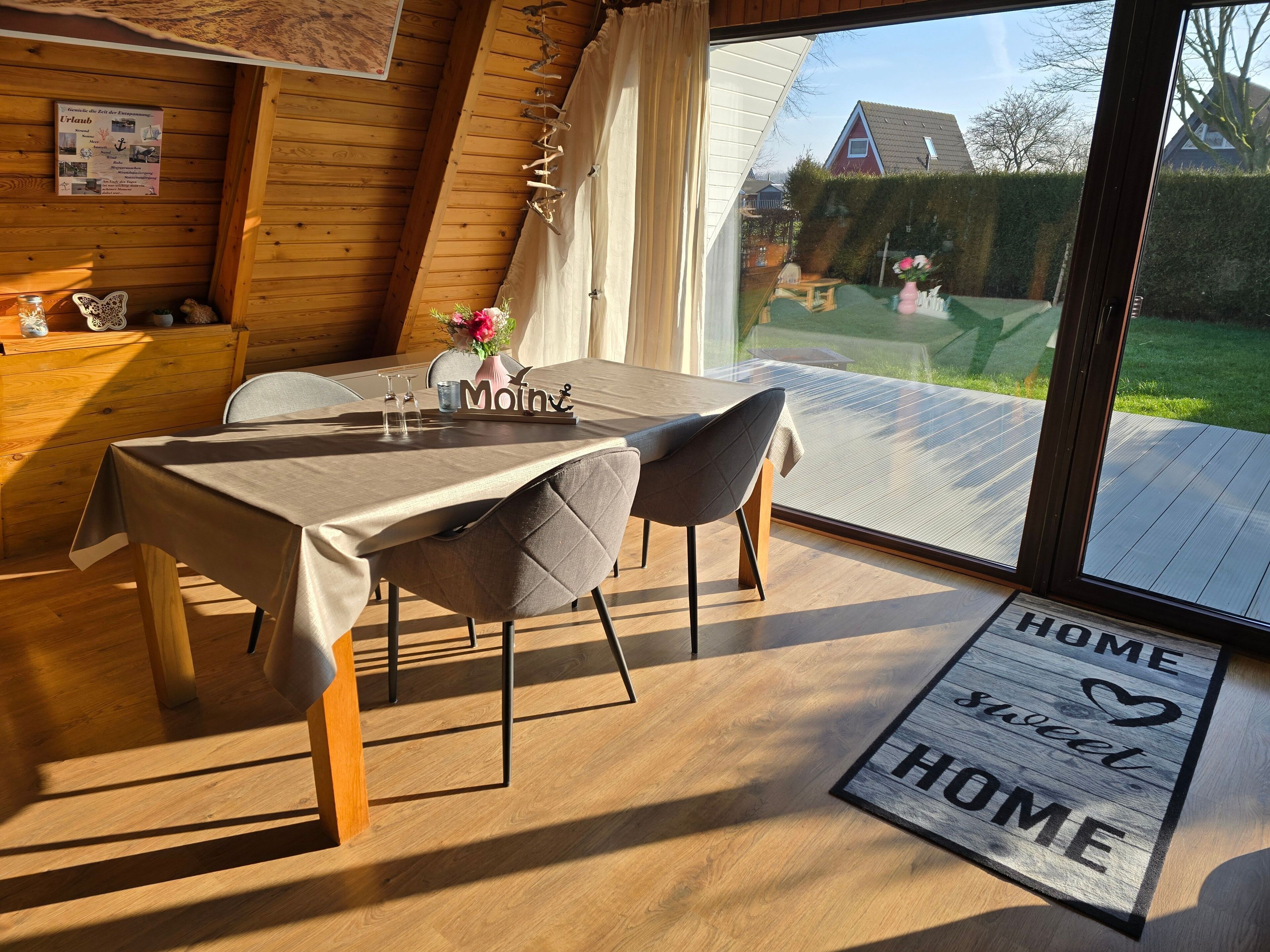 Un coin repas avec une table dressée pour deux personnes, un intérieur en bois et une vue sur le jardin grâce à de grandes fenêtres.