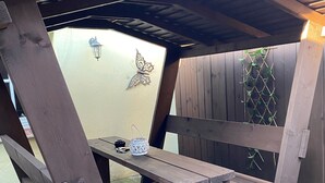 A wooden pergola with a bench, a decorative butterfly wall art, and a lattice wall with climbing plants.