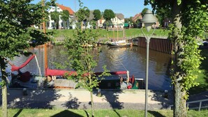 A riverside park with a small boat docked near a pedestrian bridge, surrounded by trees and buildings.