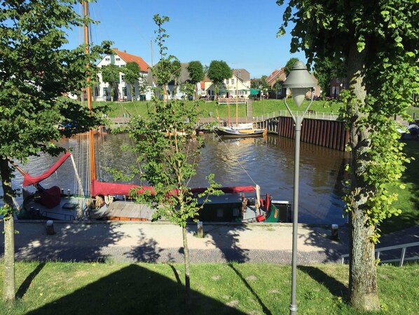 A riverside park with a small boat docked near a pedestrian bridge, surrounded by trees and buildings.