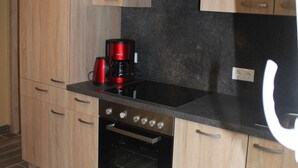 A kitchen with wooden cabinets, a black countertop, a red coffee maker, and an oven.