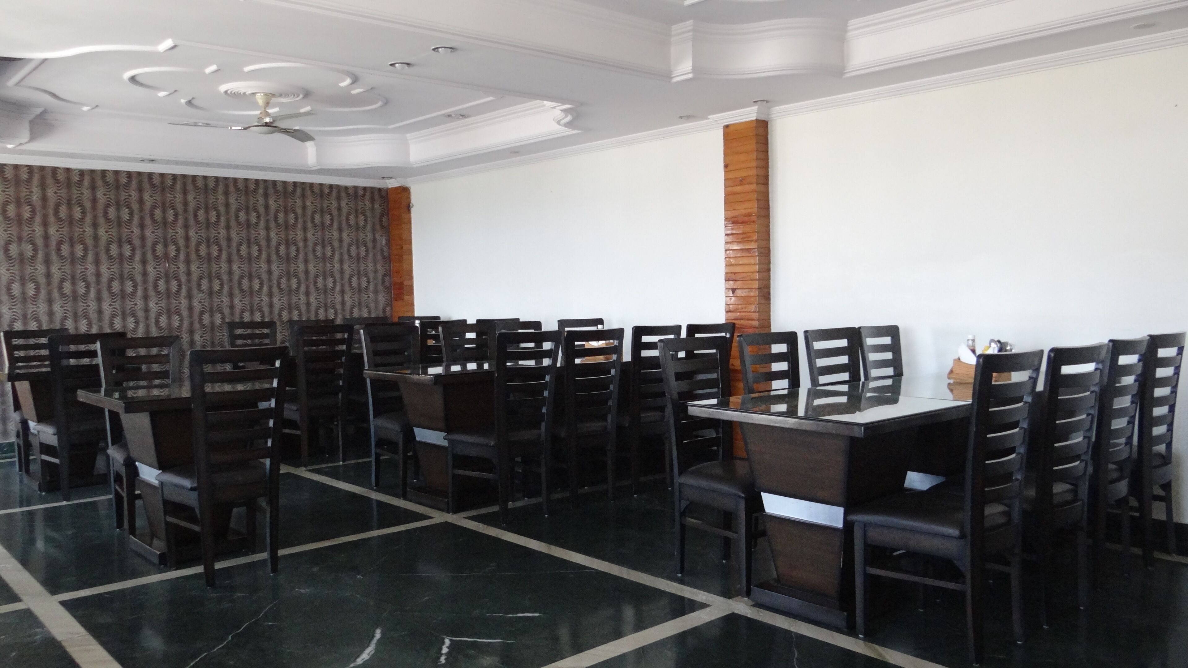 A dining area with a long table and multiple chairs, a patterned curtain, a ceiling fan, and a brick column.